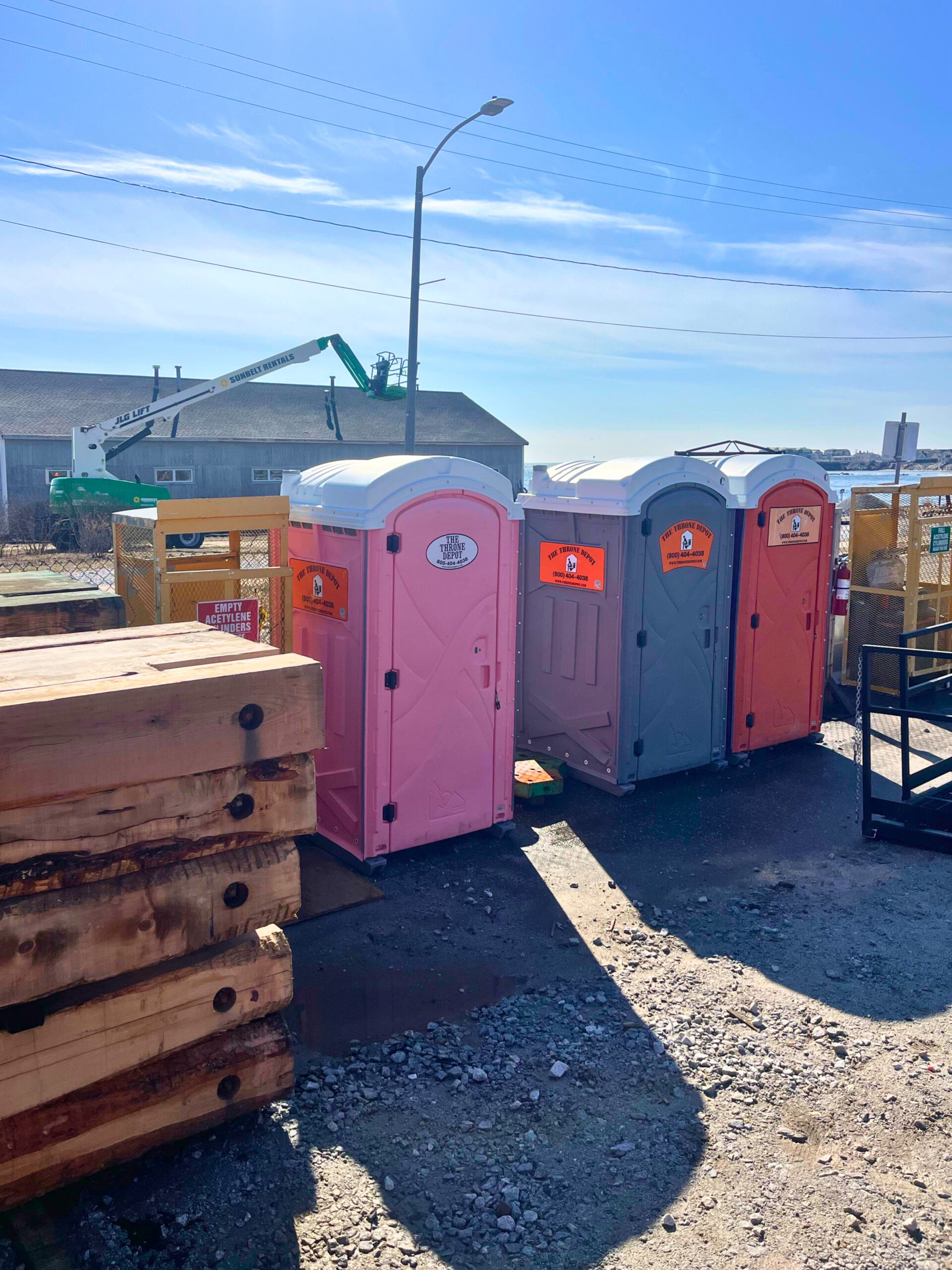 Multiple portable toilets at a construction site, including a pink portable restroom option